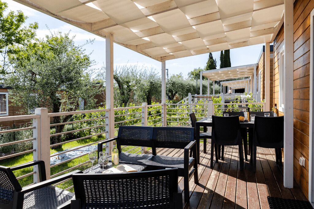 Een terras buiten met houten vloer, zwarte rieten meubels en een witte balustrade.