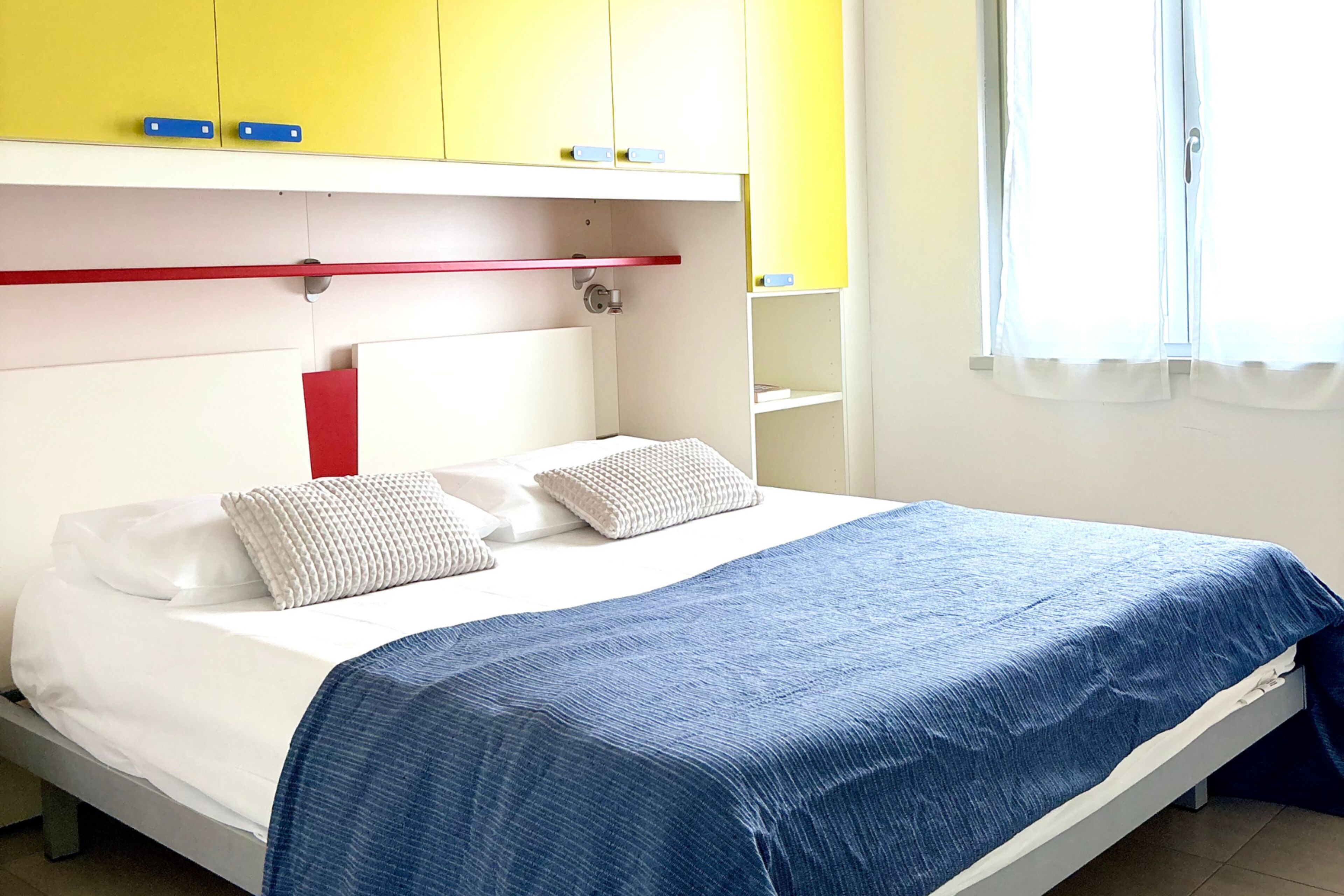 Un lit avec une couvre-lit bleue, des oreillers blancs et une tête de lit rouge.