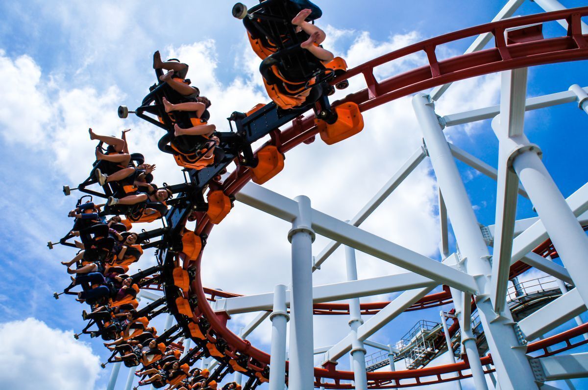 A roller coaster with riders in orange seats, white structural supports, and a clear blue sky.