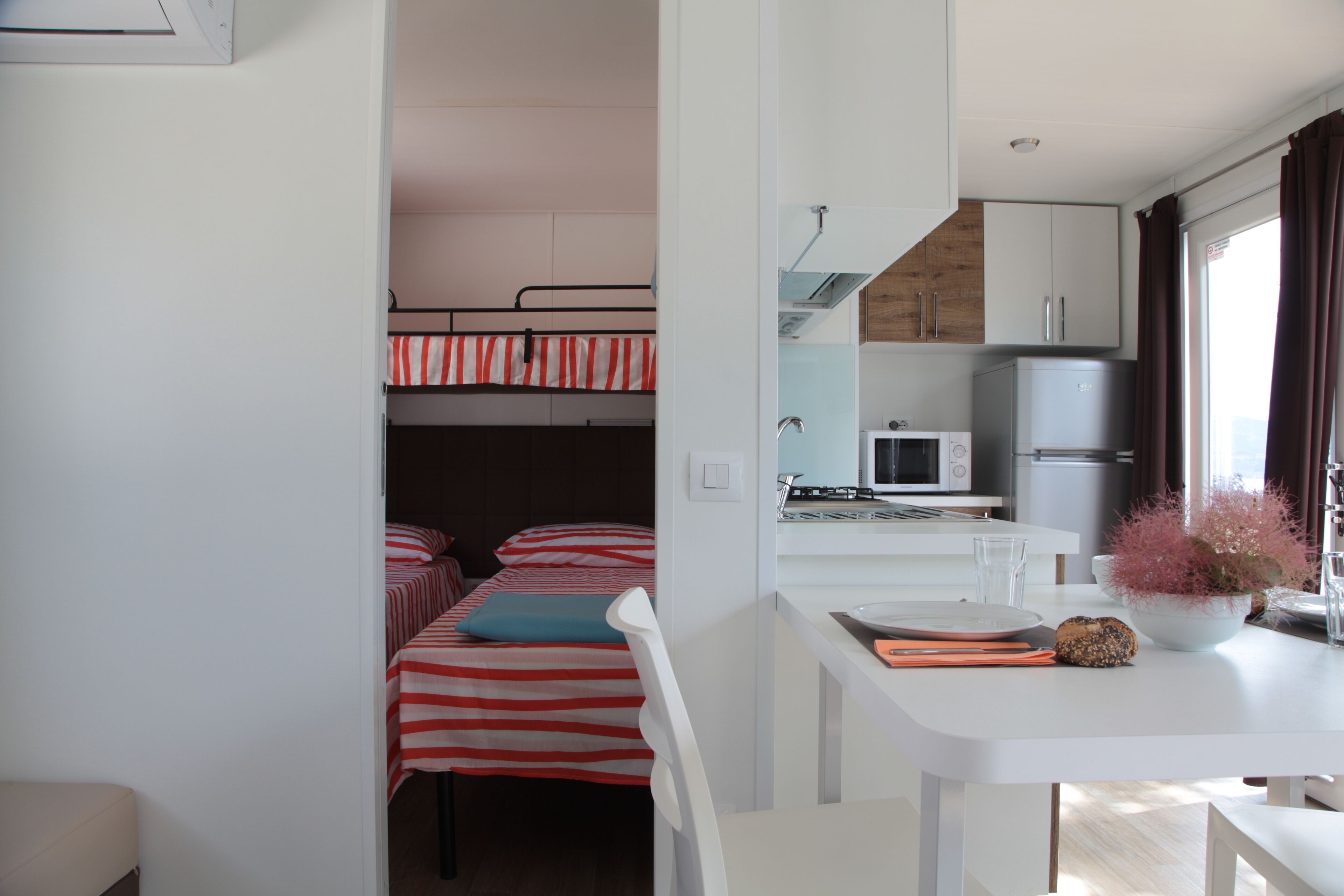 A compact room with a bunk bed, a kitchenette with a microwave, and a dining area with a table and chairs.