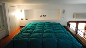 Un dormitorio con una cama grande, suelo de madera, un armario blanco y una ventana con vistas.