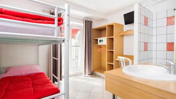 A bunk bed with red bedding, a wooden cabinet, a white chair, a sink, and a tiled wall.