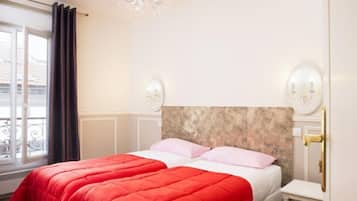 Une chambre d’hôtel avec un lit, une table de chevet, un lustre et une fenêtre avec des rideaux.