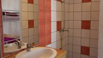 A bathroom with a wooden vanity, a white sink, a mirror, and a shower area with tiled walls.