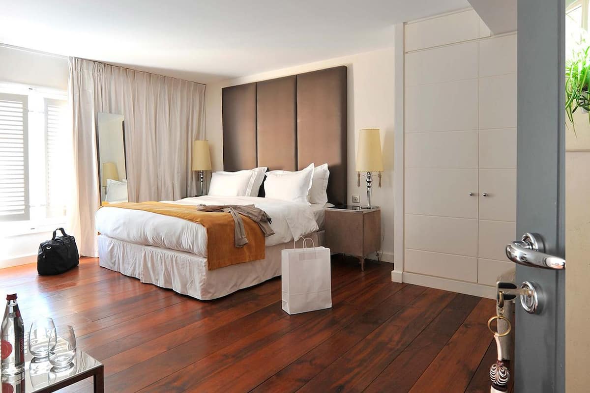 Habitación de hotel con una cama grande, mesitas de noche con lámparas, un armario y suelo de madera.