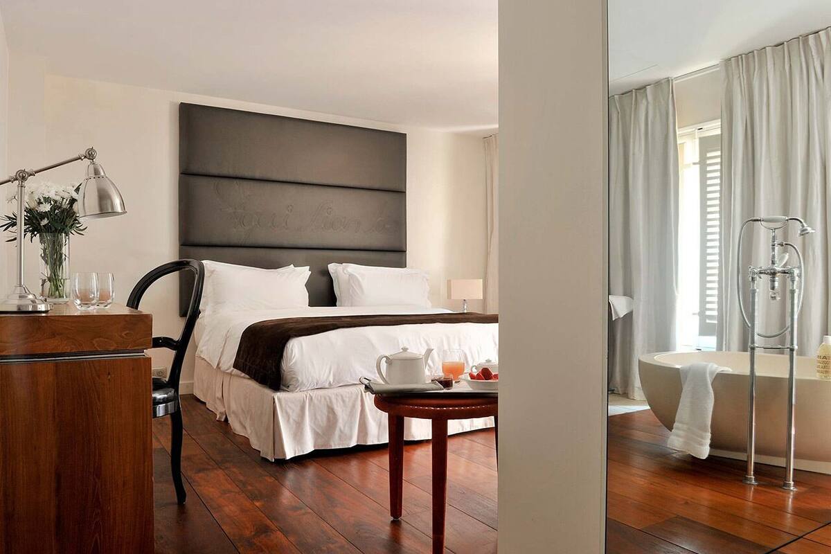 Habitación de hotel con una cama grande, mesita de noche, lámpara y baño con bañera y ducha.