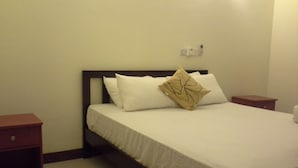 A neatly made bed with white linens and a decorative pillow, a wooden nightstand to the left, and a wall-mounted light fixture above the bed. - Apartment by the Sea - Sea Ezta by Otium (Colombo)