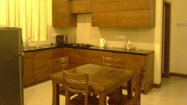 A compact kitchen with wooden cabinets, a microwave, and a dining table with chairs. - Apartment by the Sea - Sea Ezta by Otium (Colombo)