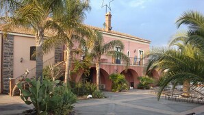 A courtyard with a building featuring a tiled roof, arches, and palm trees. - Agriturismo Masseria Portiere Stella (Paterno)