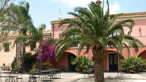 A courtyard with palm trees, outdoor seating, and a building with a tiled roof and arched doorways. - Agriturismo Masseria Portiere Stella (Paterno)