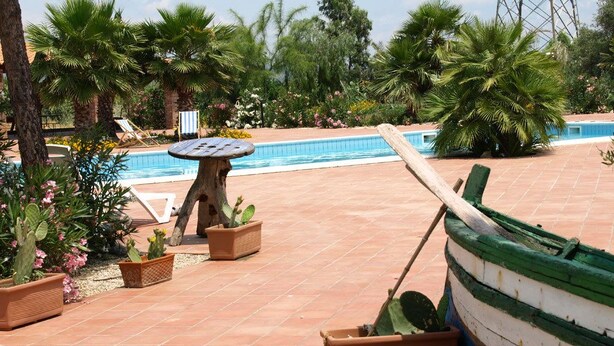 A pool area with a boat, lounge chairs, and potted plants. - Agriturismo Masseria Portiere Stella (Paterno)