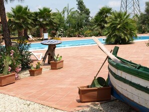 A pool area with a boat, lounge chairs, and potted plants. - Agriturismo Masseria Portiere Stella (Paterno)
