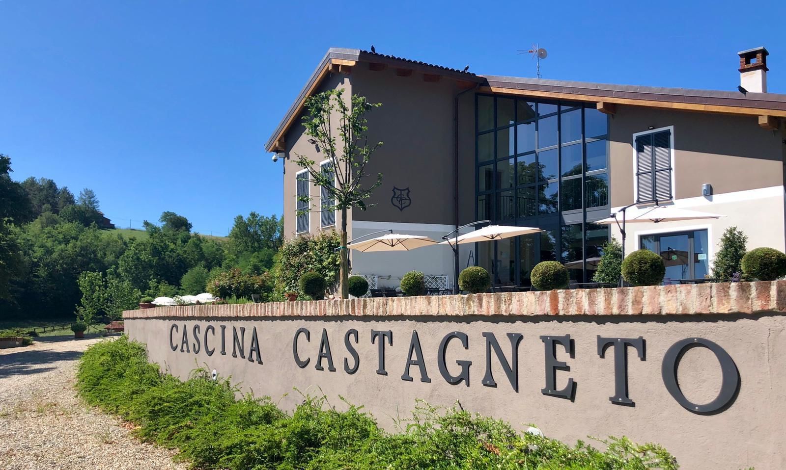 Ein Gebäude mit einem Schild, auf dem "CASCINA CASTAGNETO" steht, und einer Terrasse mit Sonnenschirmen.