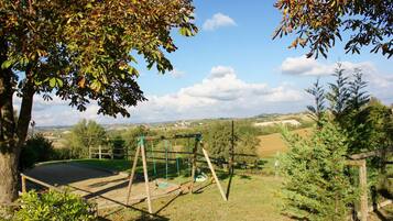 Relax in a serene outdoor setting surrounded by lush greenery and a clear sky, with a swing set and fenced play area.