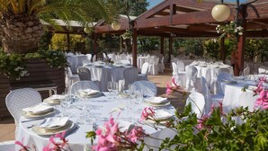 An outdoor dining area with round tables set for a meal, surrounded by white chairs and covered with white tablecloths. - La Cantinella (Ostra)