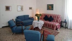 Un salon avec un canapé bleu, un canapé rouge à motifs, une petite table ronde sur laquelle est posé un vase, et un lustre.