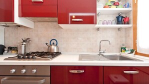 Une cuisine avec des meubles de rangement rouges, un évier en acier inoxydable et une cuisinière à gaz.