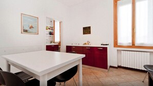 Une cuisine avec une table blanche, des placards rouges et une fenêtre avec des rideaux.