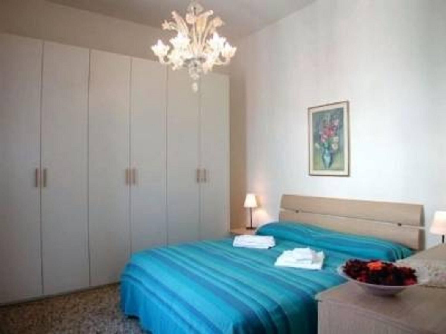 Une chambre à coucher avec un lit, un lustre, un tableau et une table de chevet sur laquelle se trouve un bol de fruits.