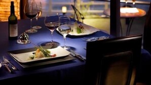 Une table à manger avec vue sur la mer et les montagnes, une bouteille de vin et une bougie posée sur la table.