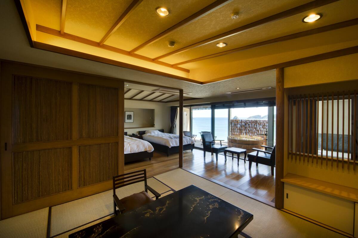 Une pièce de style japonais traditionnel, avec un sol recouvert de tatamis, une table basse et une vue sur la mer grâce à de grandes fenêtres.