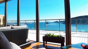 Une chambre moderne dotée d’une grande fenêtre donnant sur la mer, d’une terrasse en bois et d’un canapé.