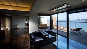 Un intérieur moderne avec une cloison en verre, une terrasse en bois dotée de sièges extérieurs et une vue sur la mer.