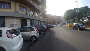 Un edificio de varios pisos con fachada curva, coches aparcados a lo largo de la calle y una acera para peatones.