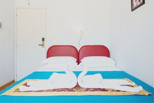 Una cama con cabeceros rojos, una colcha azul y amarilla, y toallas blancas dispuestas en forma de corazón.