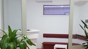 Una habitación con piso de madera, un sofá rojo, una mesita blanca y una planta en maceta.