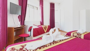 Habitación de hotel con cama, escritorio, silla, televisor y ventana con cortinas.