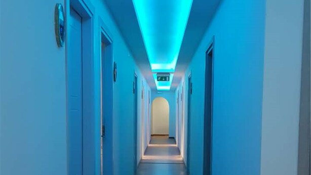 Un pasillo largo y estrecho con techo iluminado en azul y suelo de madera.
