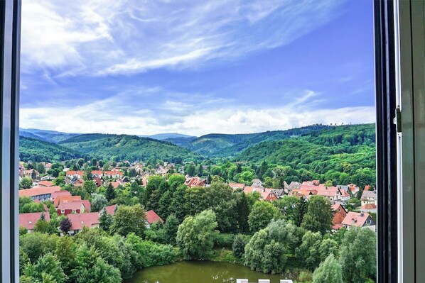 Blick auf eine Stadt mit roten Dächern, umgeben von üppiger Vegetation und Hügeln im Hintergrund.