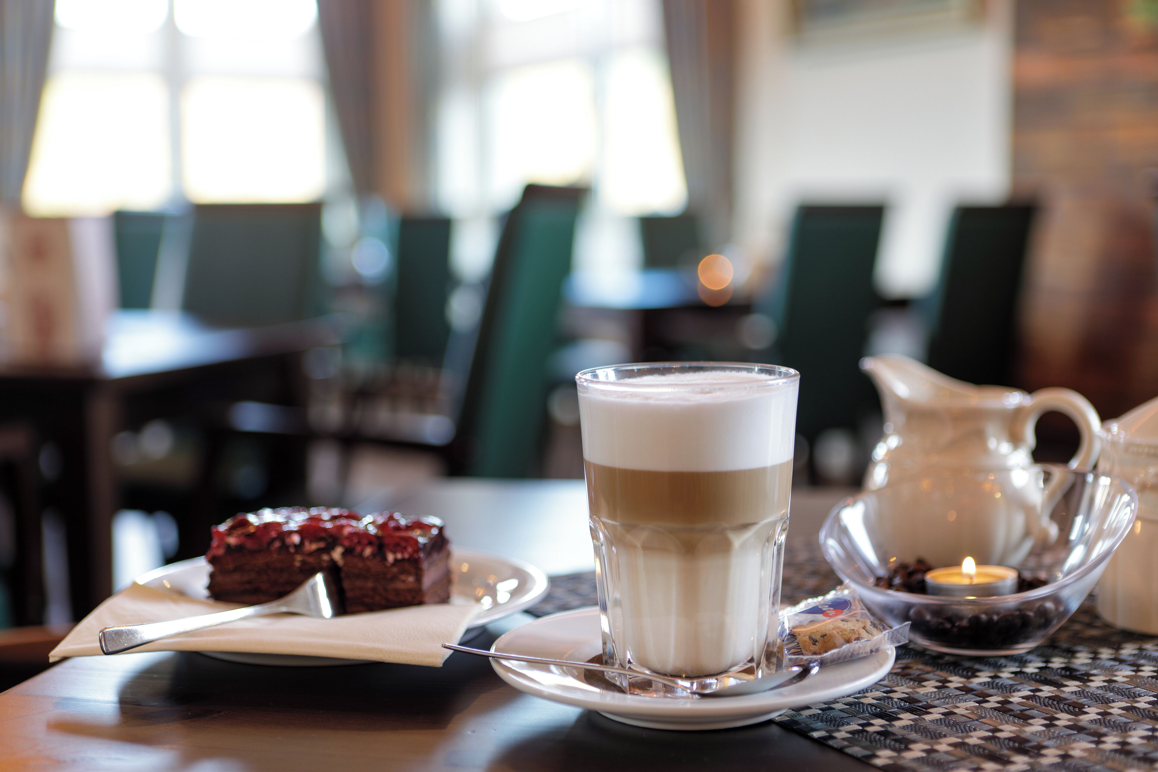 Ett bord med en kopp kaffe, en bit tårta och ett ljus.