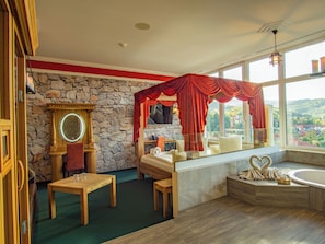 A bathroom with a stone wall, a wooden vanity, a bathtub, and a large window offering a view of a town. - Hasseröder Burghotel (Wernigerode)