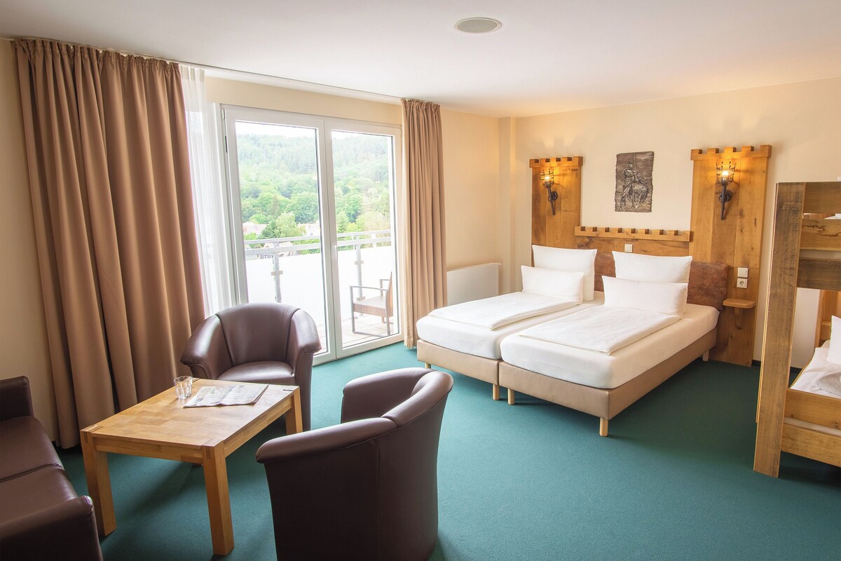 Ett hotellrum med en säng, två stolar, ett bord och utsikt över grönområden genom fönstret.