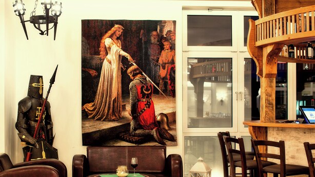 A room with a wooden barrel coffee table, leather sofas, a wooden bar with stools, and a large historical painting on the wall. - Hasseröder Burghotel (Wernigerode)