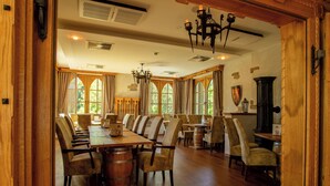 A dining area with wooden tables and chairs, a chandelier, and large windows. - Hasseröder Burghotel (Wernigerode)
