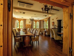 A dining area with wooden tables and chairs, a chandelier, and large windows.