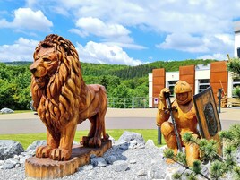 A wooden lion and knight sculpture in front of a modern building with a parking sign.