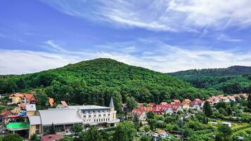 A town with a prominent building featuring a large, curved roof and a tower, surrounded by houses with red roofs and lush greenery.