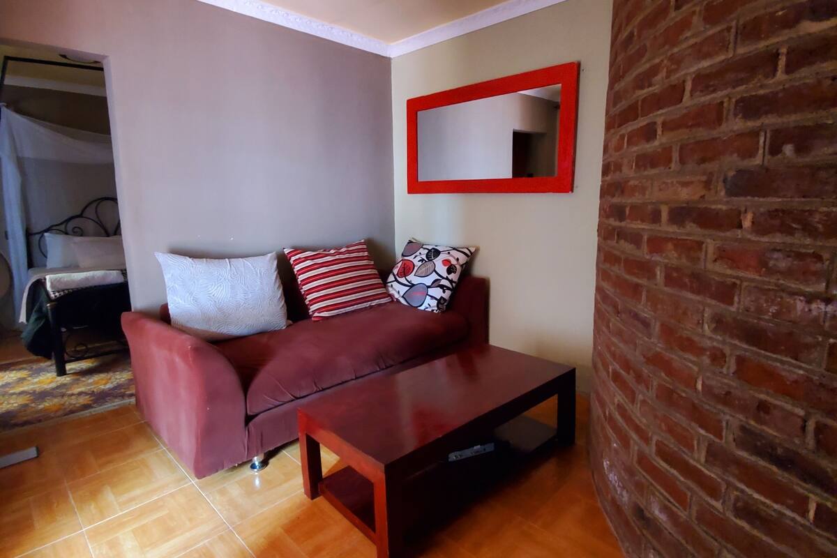 Um espaço de estar compacto com um sofá vermelho, uma pequena mesa de centro de madeira e um espelho com moldura vermelha na parede.