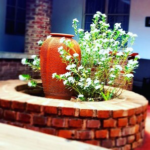 A brick planter with white flowers and a textured orange vase.