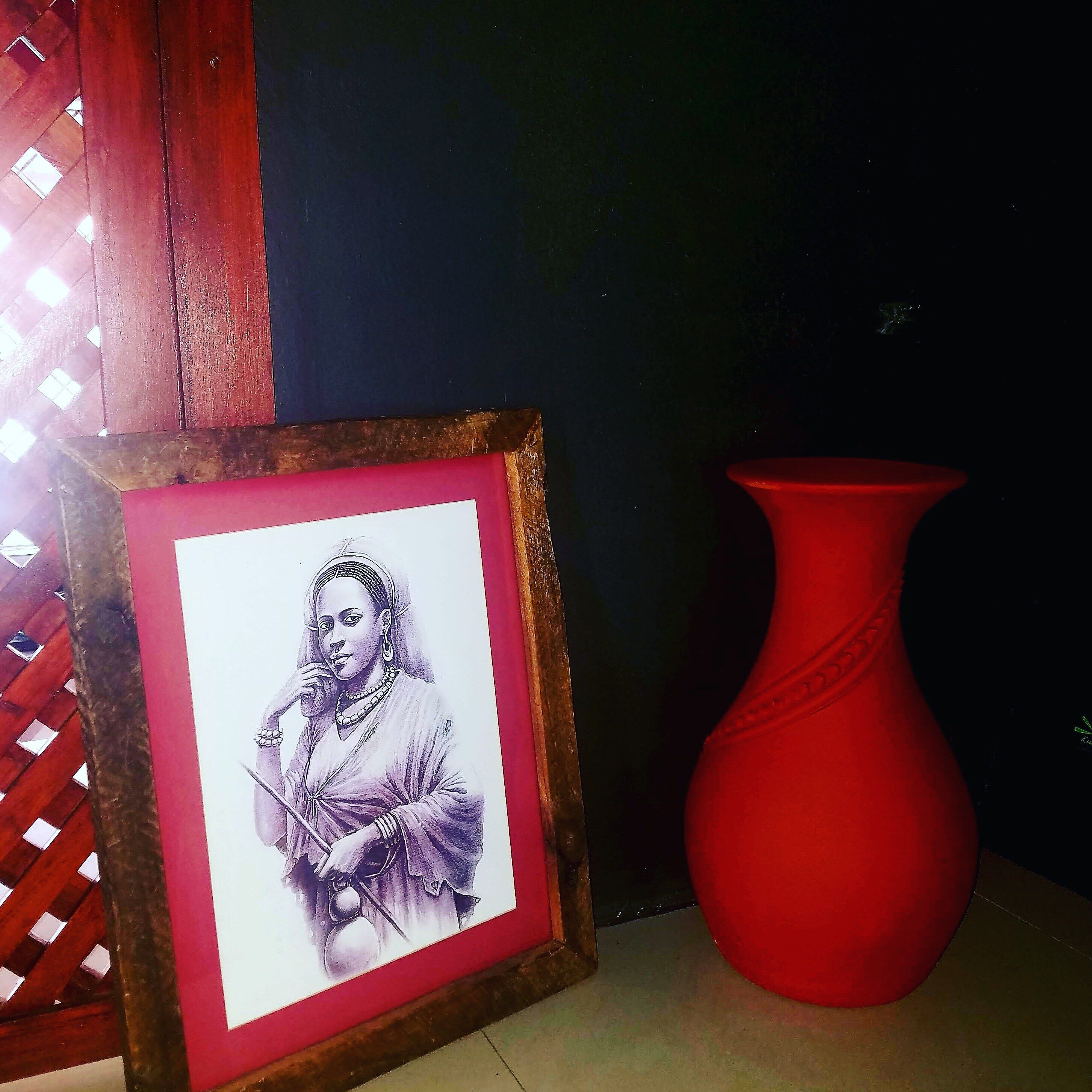 A framed drawing of a person holding a fan, a red vase, and a wooden structure with a lattice design.