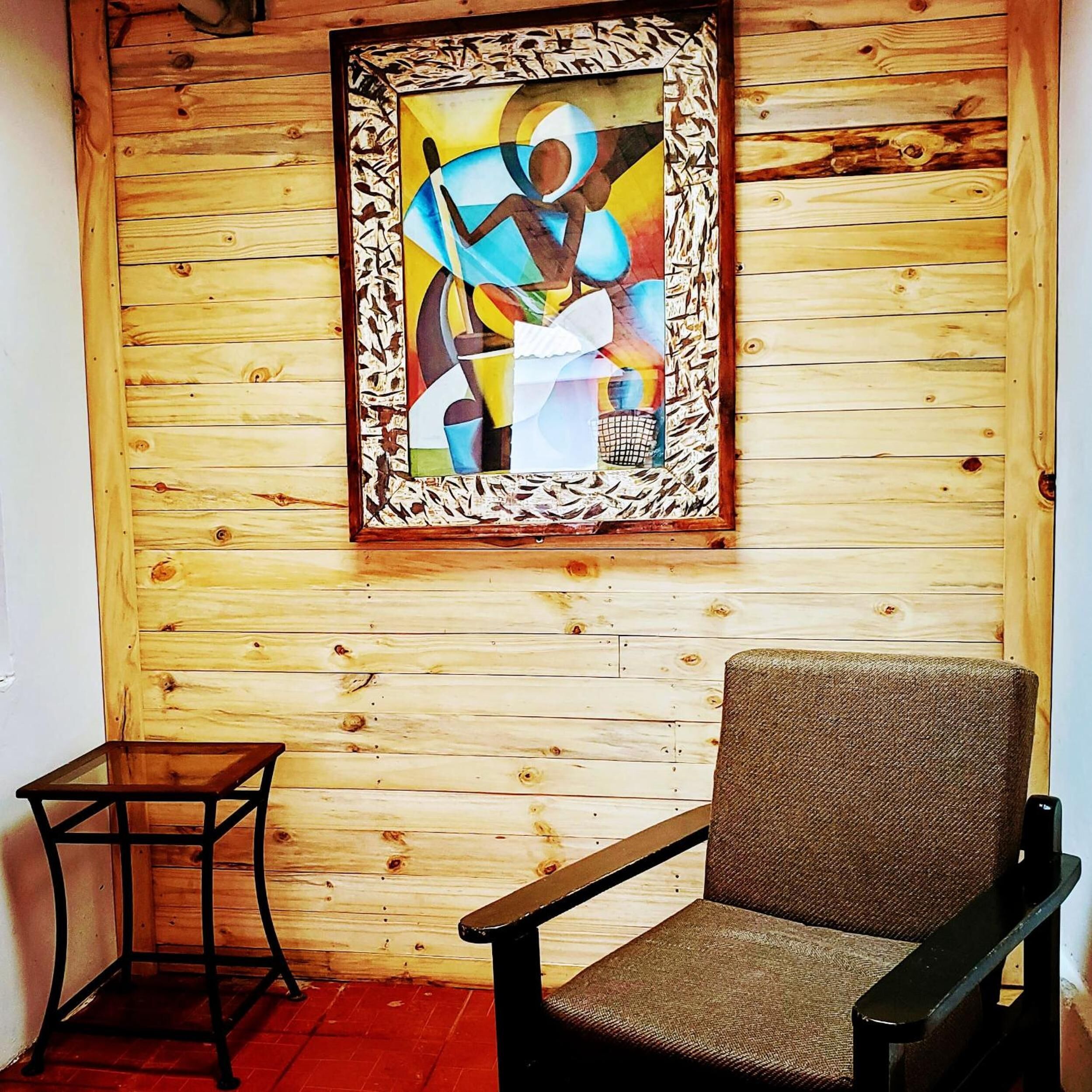 A room with a wooden slat wall, a framed abstract painting, a brown chair, and a small table.