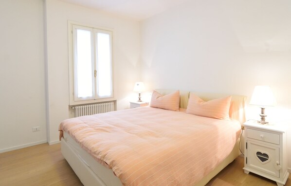 A bedroom with a bed, two bedside tables, a window, and a radiator. - Al Campaniel Apartment (Venice)