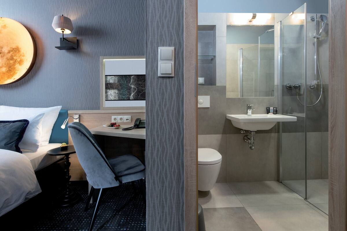 A hotel room with a bed, desk, chair, and a bathroom with a shower, sink, and toilet.
