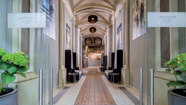 A hotel corridor with a patterned carpet, two potted plants, and a sign reading "Leonardo Boutique Hotels". - Leonardo Boutique Hotel Krakow Old Town (Kraków)