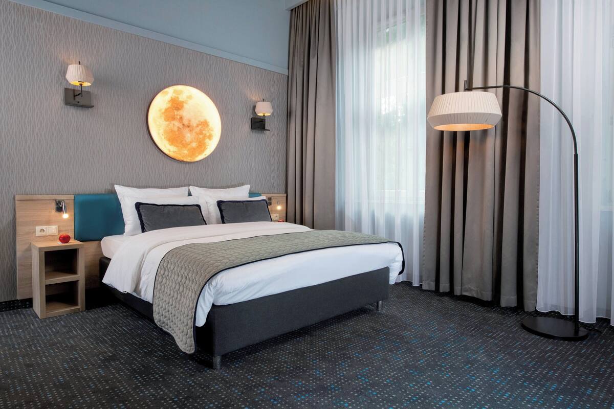 Une chambre d’hôtel moderne avec un grand lit, deux tables de chevet, une lampe sur pied et une lampe fixée au mur.