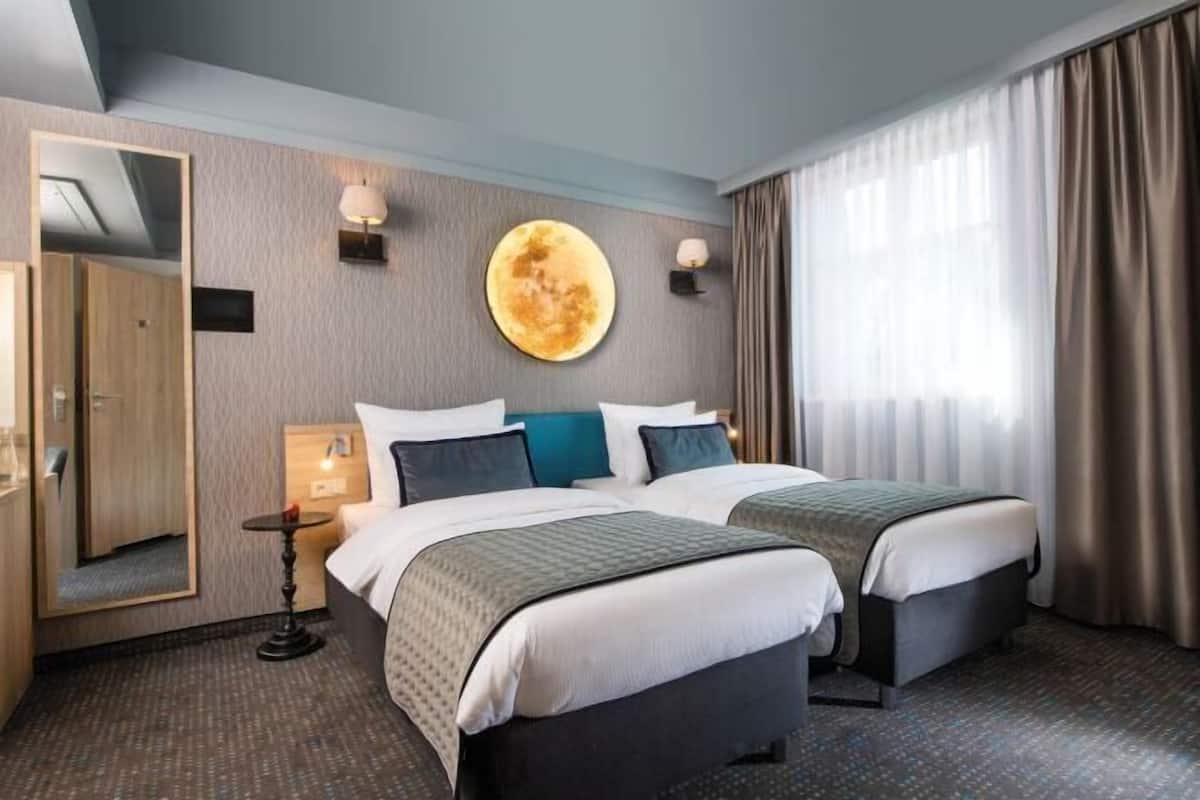 A hotel room with two beds, a large mirror, a wall clock, and a window with curtains.